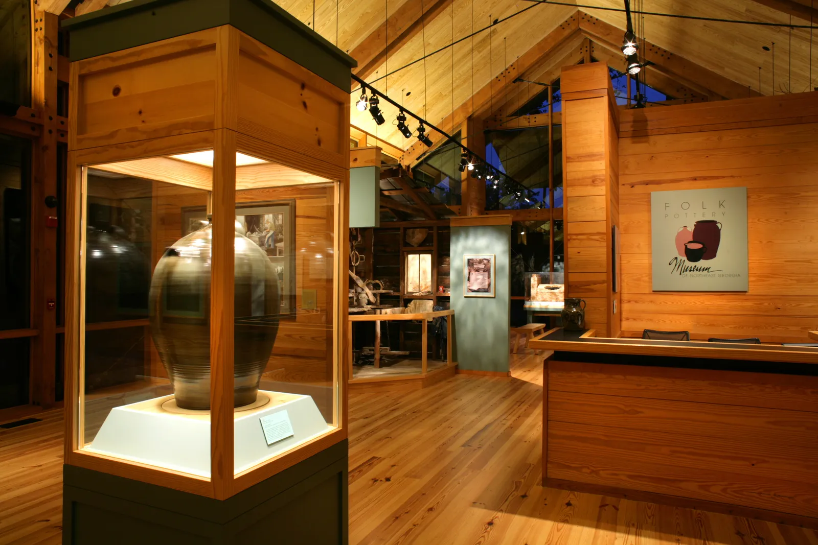 Interior of the Folk Pottery Museum showing a large glazed stoneware jar in a lighted display case beneath exposed timber-frame ceilings