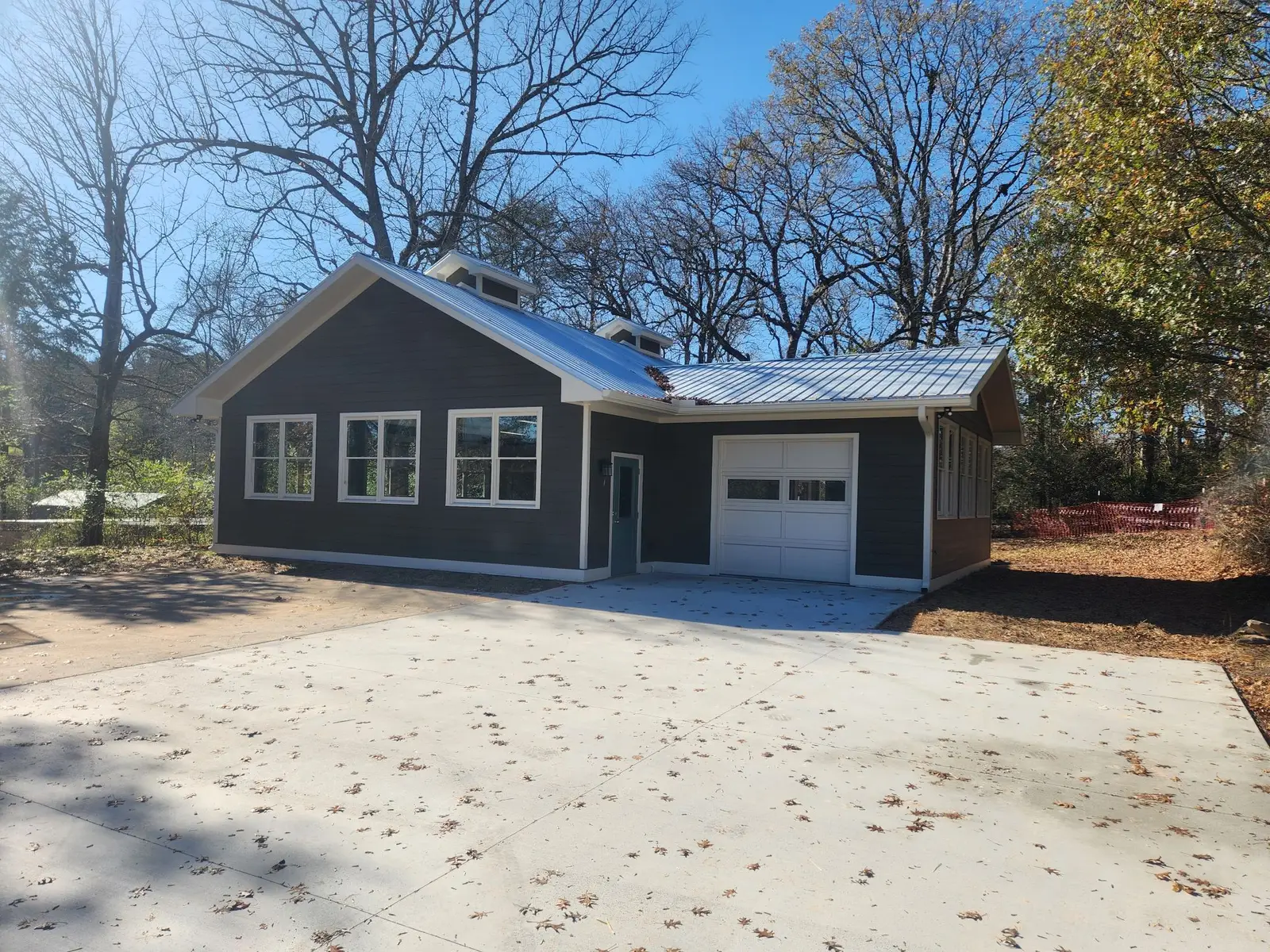 The John Burrison Pottery Studio, a new gray clapboard building with white-trimmed windows, twin roof cupolas, and a metal roof among bare oaks